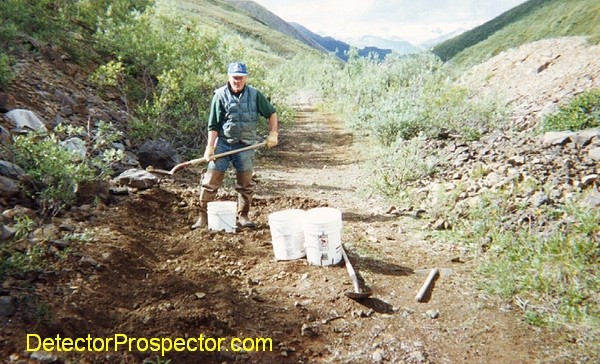 Bud Herschbach shoveling gold bearing dirt along edge of trail